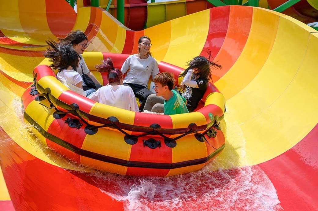 Riders on a large round CPI Amusement raft descending a water park slide